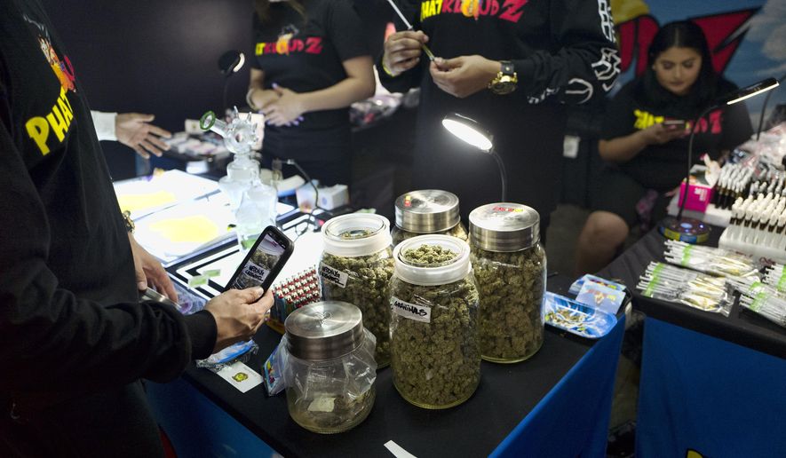 File - In this Friday, April 5, 2019, file photo, a customer takes a photo of large jars of marijuana from on display for sale at Rev-Up a cannabis marketplace in Los Angeles. California is trying a new strategy to cut into the state&#39;s huge illegal marijuana market. State regulators have proposed rules that would require legal shops to post their unique quick response code certificates in storefront windows to help consumers identify licensed businesses. Shoppers would use their smartphones to scan the familiar, black-and-white codes, similar to a bar code, to determine if a business is selling legal, tested cannabis products. (AP Photo/Richard Vogel, File)