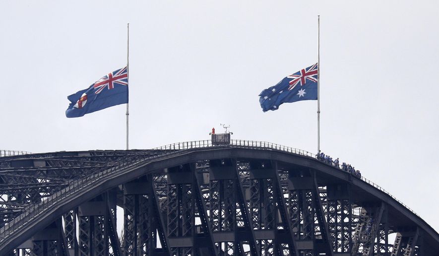 People climbing the Sydney Harbour Bridge stop under flags flying at half-mast as mark of mourning and respect in Sydney, Australia, Friday, Jan. 24, 2020, for three U.S. crew members of an aerial water tanker that crashed Thursday while battling wildfires in Australia. (AP Photo/Rick Rycroft)