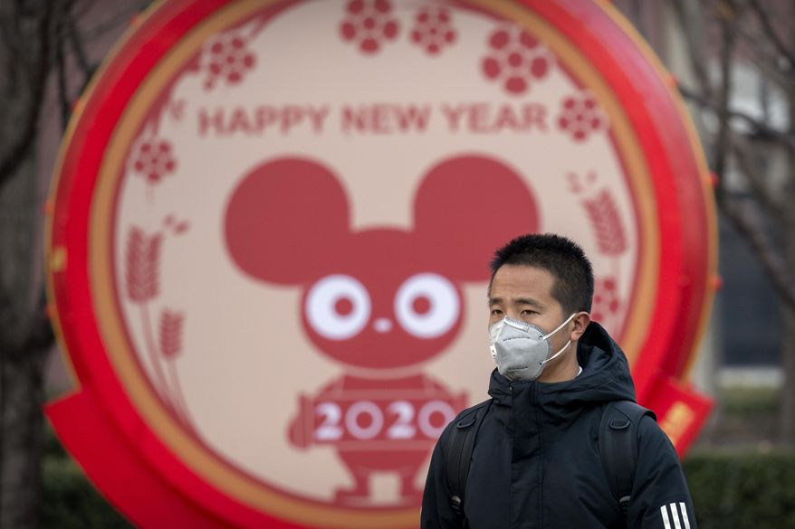 FILE - In this Jan. 22, 2020 photo, a man wears a face mask as he walks past a display for the upcoming Lunar New Year, the Year of the Rat, in Beijing, Wednesday, Jan. 22, 2020. A virus that has killed more than two dozen people and sickened hundreds more has all but shut down China&#39;s biggest holiday of the year, the Lunar New Year. Instead of family reunions or sightseeing trips, many of the country&#39;s 1.4-billion people are hunkering down as the country scrambles to prevent the illness from spreading further. (AP Photo/Mark Schiefelbein, File)
