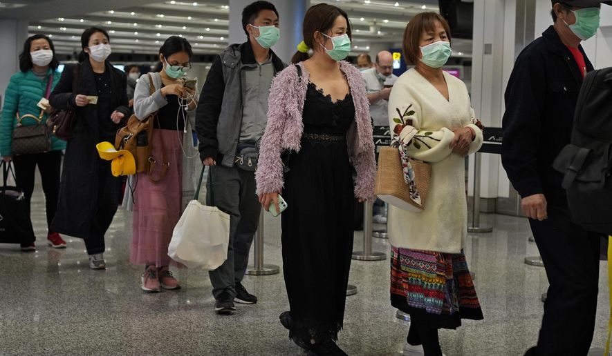 Passengers wear masks as they walk at the Hong Kong International Airport in Hong Kong Saturday, Jan. 25, 2020. Hong Kong has declared the outbreak of a new virus an emergency and will close primary and secondary schools for two more weeks after the Lunar New Year holiday. City leader Carrie Lam also announced Saturday that trains and flights from the city of Wuhan would be blocked. (AP Photo/Vincent Yu)