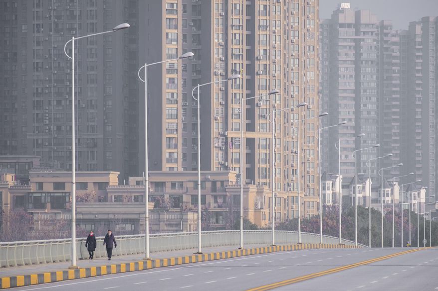 People wearing face masks walk down a deserted street in Wuhan in central China's Hubei Province, Tuesday, Jan. 28, 2020. China's death toll from a new viral disease that is causing a global concern rose by 25 to at least 106 on Tuesday as the United States and other governments prepared to fly their citizens out of the locked-down city at center of the outbreak. (AP Photo/Arek Rataj)