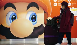 In this Jan. 23, 2020, photo, a traveler walks past a propaganda featuring Nintendo character at Narita airport in Narita, near Tokyo. Japanese video game maker Nintendo is reporting a 29% rise in quarterly profit on solid demand for its Switch console during the year-end shopping season.  (AP Photo/Eugene Hoshiko)