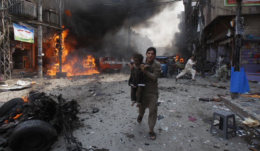 In this Sept. 29, 2013, file photo, a Pakistani man carrying a child rushes away from the site of a blast shortly after a car bomb exploded in Peshawar, Pakistan. (AP Photo/Mohammad Sajjad, File)