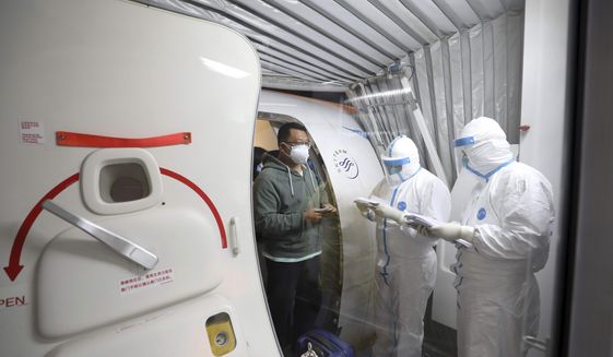 Quarantine workers in protective suits check identity documents as tourists from the Wuhan area walk off of a chartered plane taking them home from Bangkok at Wuhan Tianhe International Airport in Wuhan in central China&#39;s Hubei Province, Friday, Jan. 31, 2020. A group of Chinese tourists who have been trapped in Thailand since Wuhan was locked down due to an outbreak of new virus returned to China on Friday. (Chinatopix via AP)