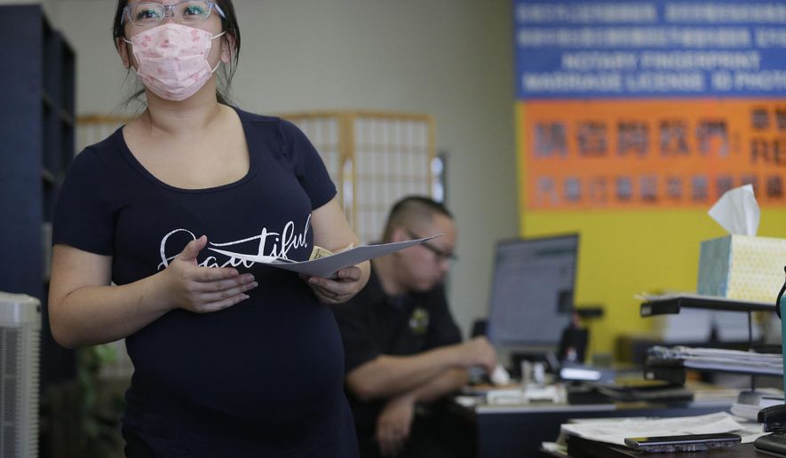 Employee Cynthia Bao, who is pregnant wears a protective mask to avoid getting sick, as she interacts with customers at the Beyond Services notary in Alhambra, Calif., Friday, Jan. 31, 2020. As China grapples with the growing coronavirus outbreak, Chinese people in the Los Angeles area, home to the third-largest Chinese immigrant population in the United States, are encountering a cultural disconnect as they brace for a possible spread of the virus in their adopted homeland. (AP Photo/Damian Dovarganes)