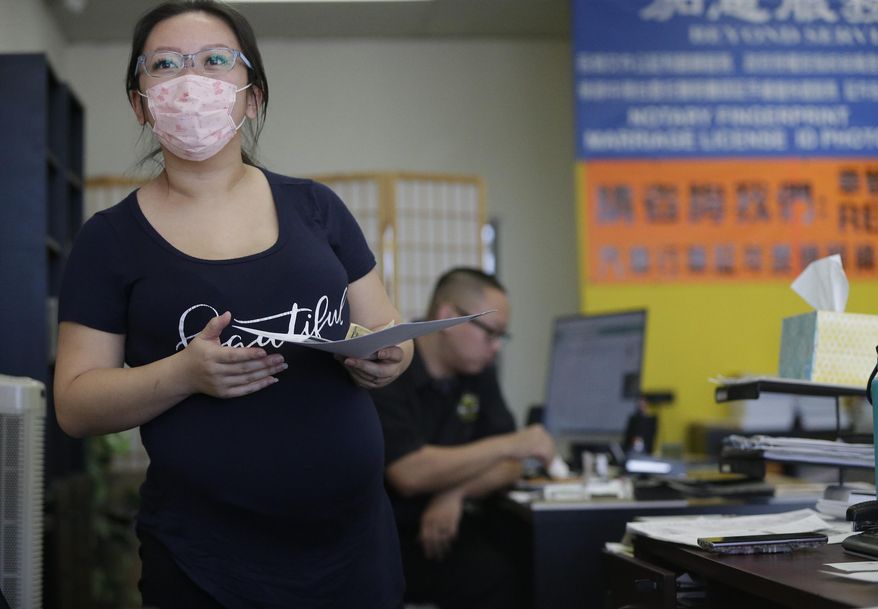 Employee Cynthia Bao, who is pregnant wears a protective mask to avoid getting sick, as she interacts with customers at the Beyond Services notary in Alhambra, Calif., Friday, Jan. 31, 2020. As China grapples with the growing coronavirus outbreak, Chinese people in the Los Angeles area, home to the third-largest Chinese immigrant population in the United States, are encountering a cultural disconnect as they brace for a possible spread of the virus in their adopted homeland. (AP Photo/Damian Dovarganes)