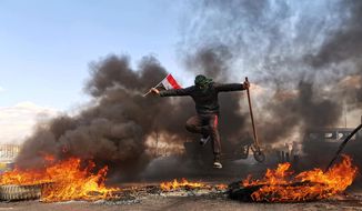 An anti-government protester jumps over burning tires blocking a street during a demonstration against the newly appointed Prime Minister Mohammed Allawi in Najaf, Iraq, Sunday, Feb. 2, 2020. Former communications minister Mohammed Allawi was named prime minister-designate by rival Iraqi factions Saturday after weeks of political deadlock. (AP Photo/Hadi Mizban)