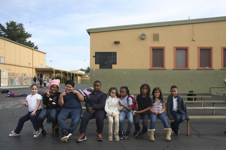 In this Jan. 27, 2020, photo, students at Lake Elementary School in San Pablo, Calif., sit on a bench in the schoolyard. The school was built in the 1950s and still has its old linoleum tiles that contain asbestos and other potentially harmful relics of the past. Proposition 13, the only statewide measure on the March 3 ballot, would create a $15 billion bond to build, repair and modernize schools, from kindergarten through public colleges and universities. (AP Photo/Jocelyn Gecker)