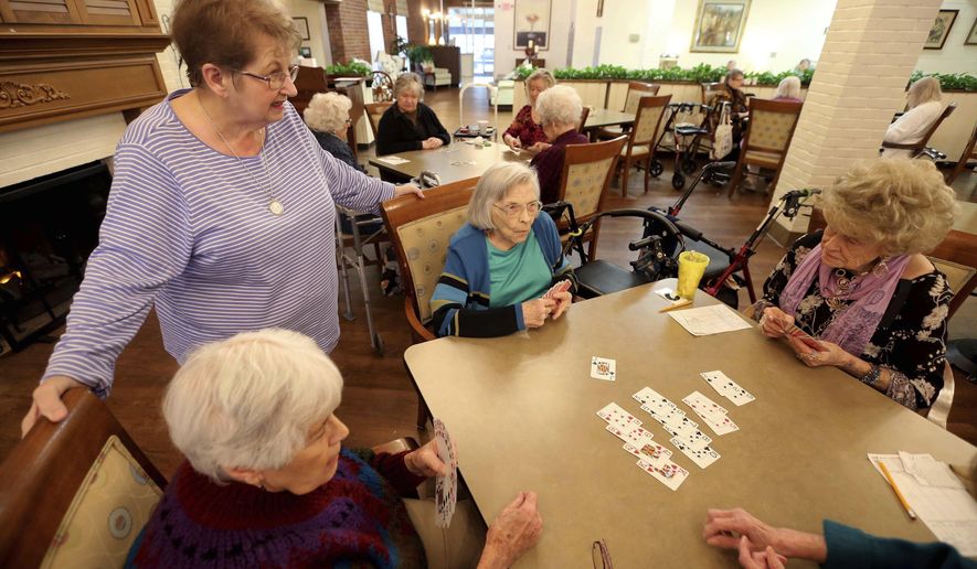 In this Thursday, Jan. 23, 2020, photo, bridge hostess Mary Vlach, standing, visits with a table of bridge players at raceway Retirement Community in Tupelo, Miss. The hostess does all the calling to see who’s coming, arrives early to set up the tables and fills in at a table if they need a sub,” said Vlach, 75. (Adam Robison/The Northeast Mississippi Daily Journal via AP)