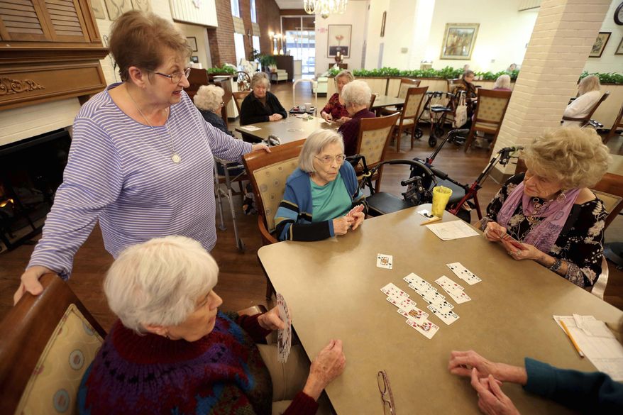 In this Thursday, Jan. 23, 2020, photo, bridge hostess Mary Vlach, standing, visits with a table of bridge players at raceway Retirement Community in Tupelo, Miss. The hostess does all the calling to see who’s coming, arrives early to set up the tables and fills in at a table if they need a sub,” said Vlach, 75. (Adam Robison/The Northeast Mississippi Daily Journal via AP)