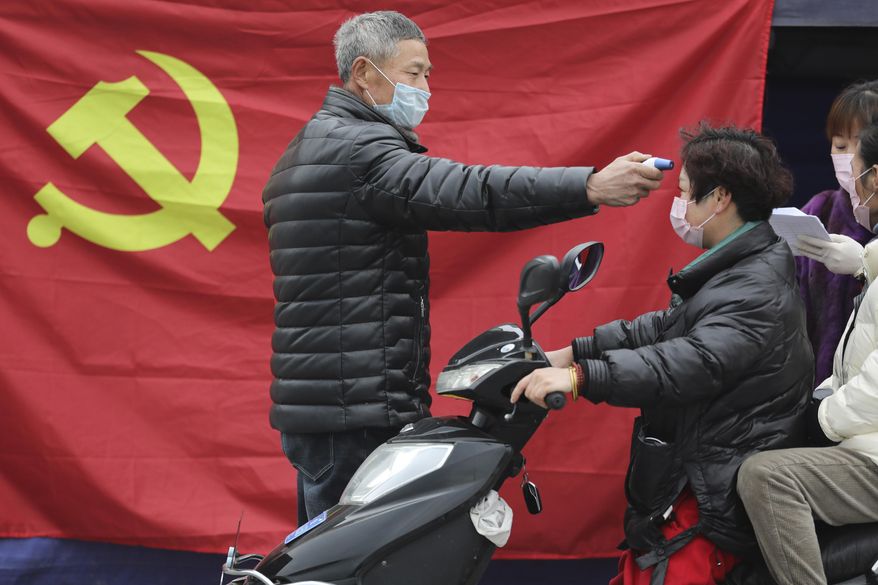 A volunteer stands in front of a Communist Party flag as he takes the temperature of a scooter driver at a roadside checkpoint in Hangzhou in eastern China&#39;s Zhejiang Province, Monday, Feb. 3, 2020. China sent medical workers and equipment to a newly built hospital, infused cash into financial markets and further restricted people&#39;s movement in sweeping new steps Monday to contain a rapidly spreading virus and its escalating impact. (Chinatopix via AP)