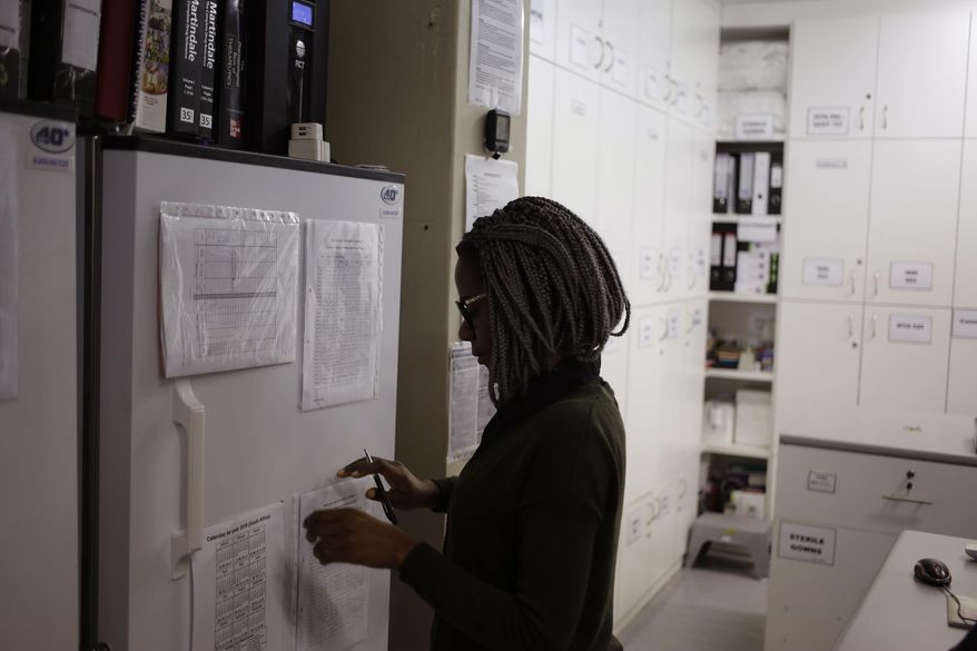 FILE - In a Nov. 30, 2016 file photo, pharmacist Mary Chindanyika looks at documents on a fridge containing a trial vaccine against HIV on the outskirts of Cape Town, South Africa. The latest attempt at an HIV vaccine has failed. Researchers announced Monday, Feb. 3, 2020 they've stopped giving the experimental shots in a major study in South Africa, which has one of the world's highest HIV rates. (AP Photo/Schalk van Zuydam, File)