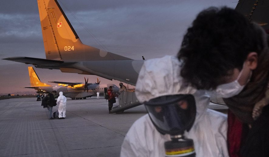 In this Feb. 2, 2020, photo, Polish military personnel wearing protective suits talk with evacuees from Wuhan, China, after their arrival at an airport in Marseilles, France. China said Tuesday the number of infections from a new virus surpassed 20,000 as medical workers and patients arrived at a new hospital and President Xi Jinping said "we have launched a people's war of prevention of the epidemic." (AP Photo/Arek Rataj)