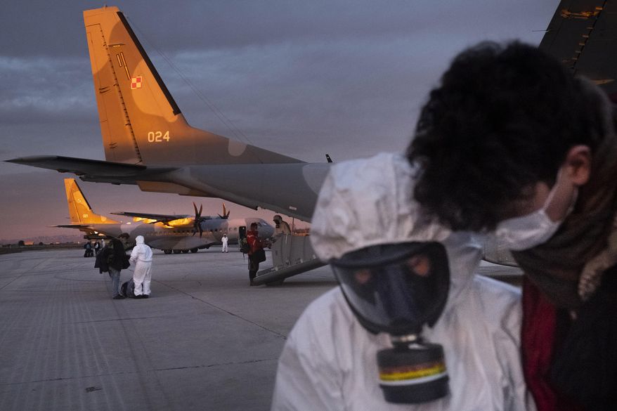 In this Feb. 2, 2020, photo, Polish military personnel wearing protective suits talk with evacuees from Wuhan, China, after their arrival at an airport in Marseilles, France. China said Tuesday the number of infections from a new virus surpassed 20,000 as medical workers and patients arrived at a new hospital and President Xi Jinping said "we have launched a people's war of prevention of the epidemic." (AP Photo/Arek Rataj)
