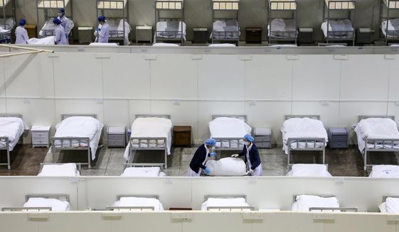 In this Wednesday, Feb. 5, 2020, photo, medical staff prepare beds at a temporary hospital which transformed from an exhibition center for accepting patients who diagnosed with the coronaviruses in Wuhan in central China&#39;s Hubei province. Ten more people were sickened with a new virus aboard one of two quarantined cruise ships with some 5,400 passengers and crew aboard, health officials in Japan said Thursday, as China reported 73 more deaths and announced that the first group of patients were expected to start taking a new antiviral drug. (Chinatopix via AP)