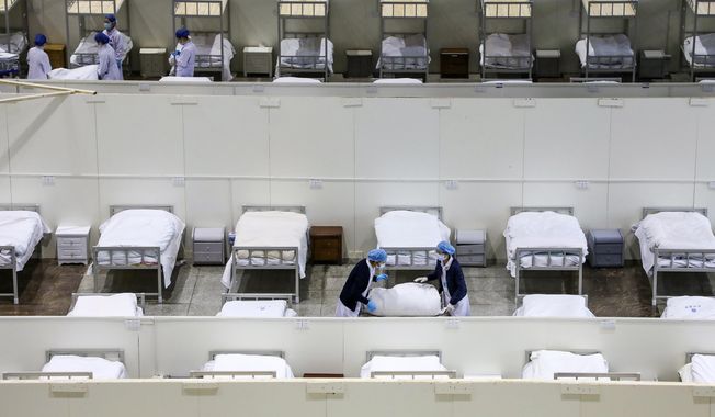 In this Wednesday, Feb. 5, 2020, photo, medical staff prepare beds at a temporary hospital which transformed from an exhibition center for accepting patients who diagnosed with the coronaviruses in Wuhan in central China&#x27;s Hubei province. Ten more people were sickened with a new virus aboard one of two quarantined cruise ships with some 5,400 passengers and crew aboard, health officials in Japan said Thursday, as China reported 73 more deaths and announced that the first group of patients were expected to start taking a new antiviral drug. (Chinatopix via AP)