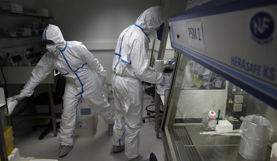 French lab scientists in hazmat gear inserting liquid in test tube manipulate potentially infected patient samples at Pasteur Institute in Paris, Thursday, Feb. 6, 2020. Scientists at the Pasteur Institute developed and shared a quick test for the new virus that is spreading worldwide, and are using genetic information about the coronavirus to develop a potential vaccine and treatments. (AP Photo/Francois Mori)