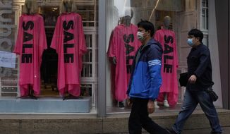 People wearing face masks walk past a fashion shop in Hong Kong, Thursday, Feb. 6, 2020. Ten more people were sickened with a new virus aboard one of two quarantined cruise ships with some 5,400 passengers and crew aboard, health officials in Japan said Thursday, as China reported 73 more deaths and announced that the first group of patients were expected to start taking a new antiviral drug. (AP Photo/Vincent Yu)