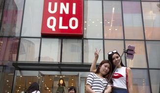 FILE - In this July 16, 2015, file photo, Chinese women take a selfie outside the Uniqlo flagship store in Beijing. Fast Retailing Co., parent of Uniqlo fashion chain, said it has temporarily closed about half of its 750 outlets in mainland China due to the outbreak of a new virus. (AP Photo/Ng Han Guan, File)