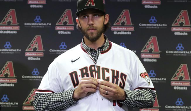 FILE - In this Dec. 17, 2019, file photo, newly acquired Arizona Diamondbacks pitcher Madison Bumgarner puts on a jersey after being introduced during a team availability in Phoenix. The Diamondbacks added a handful of veteran free agents during the offseason, including Bumgarner, outfielder Kole Calhoun, catcher Stephen Vogt and reliever Héctor Rondón. The left-handed Bumgarner — a four-time All-Star and 2014 World Series MVP — was the marquee signing, joining the rotation on an $85 million, five-year deal. (AP Photo/Matt York, File)