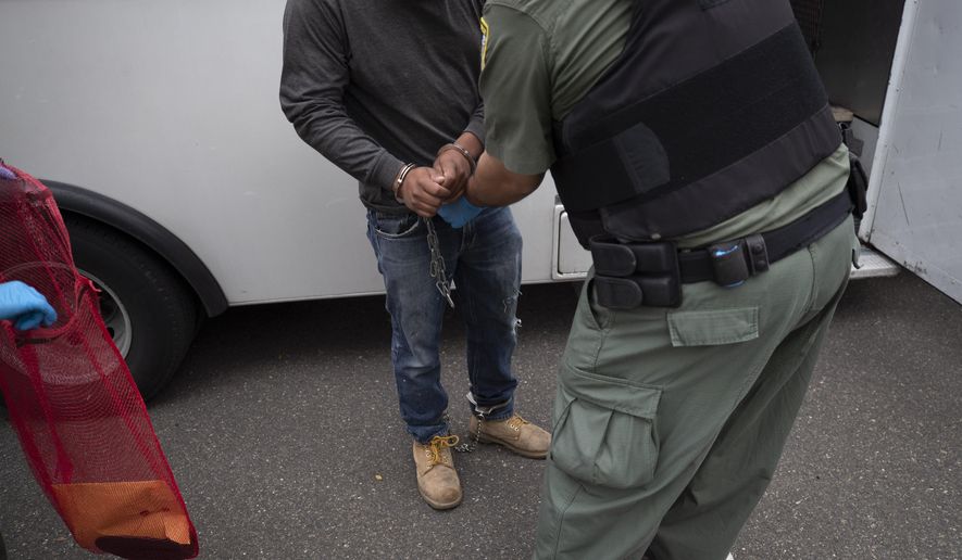 In this July 8, 2019, file photo, a U.S. Immigration and Customs Enforcement (ICE) officers transfer a man in handcuffs and ankle cuffs onto a van during an operation in Escondido, Calif. (AP Photo/Gregory Bull, File)