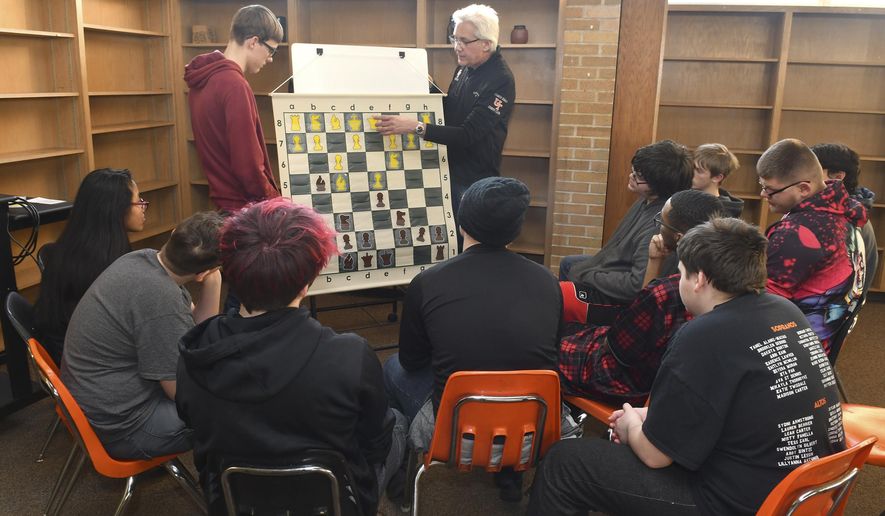 United Township student Seth Bealer and Dr. Thomas Ebalo stands with a large chess practice game board as Ebalo talks about some of the basic chess moves to United Township students during first practice at the school old library, Tuesday, Jan. 21, 2020, in East Moline, Ill. United Township high school is starting a chess club. (Gary Krambeck/Quad City Times via AP)