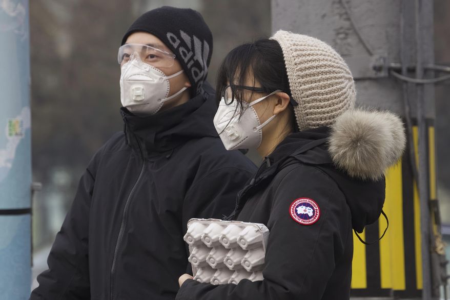 Residents wearing masks wait at a traffic light in Beijing, China Thursday, Feb. 13, 2020. China is struggling to restart its economy after the annual Lunar New Year holiday was extended to try to keep people home and contain novel coronavirus. Traffic remained light in Beijing, and many people were still working at home. (AP Photo/Ng Han Guan)