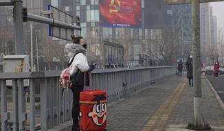 A traveler stands on a bridge near a display showing government propaganda in the fight against the COVID-19 viral illness in Beijing, China Thursday, Feb. 13, 2020. China is struggling to restart its economy after the annual Lunar New Year holiday was extended to try to keep people home and contain novel coronavirus. Traffic remained light in Beijing, and many people were still working at home. (AP Photo/Ng Han Guan)