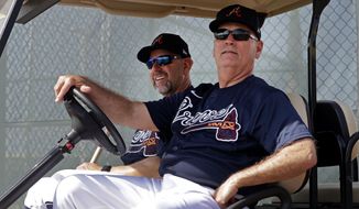 Atlanta Braves manager Brian Snitker, right, and bench coach Walt Weiss watch from a golf cart as the pitchers and catchers get loose during spring training baseball camp Thursday, Feb. 13, 2020, in North Port, Fla. (AP Photo/John Bazemore)