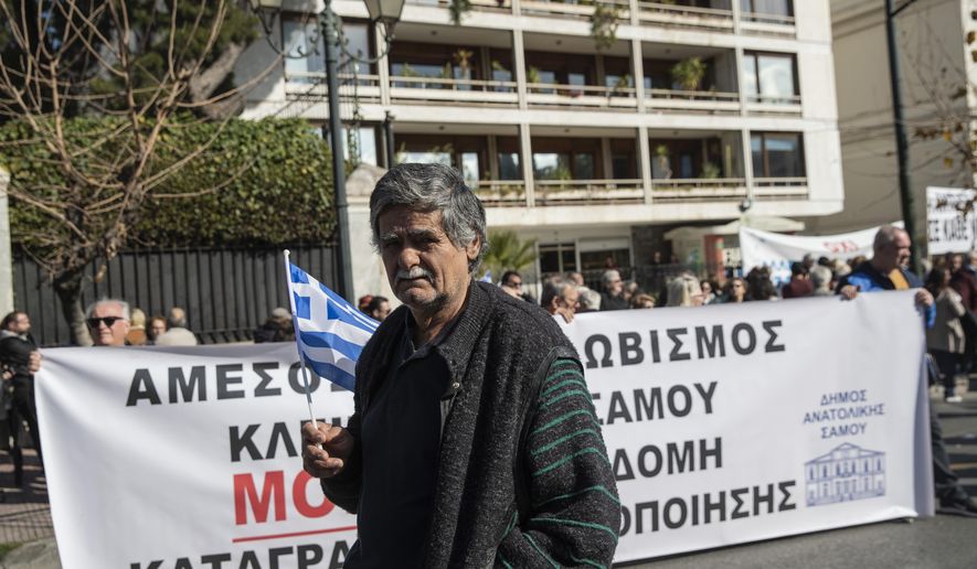 A protester holds a Greek flag during a demonstration outside the Interior Ministry in central Athens, on Thursday, Feb. 13, 2020. Regional government officials and residents from Lesbos and four other Aegean Sea islands oppose government plans to build new sites for migrants and refugees, and are demanding that thousands of asylum seekers at overcrowded camps on the islands be moved to the Greek mainland. The Moria refugee camp on the island of Lesbos currently has more than 20,000 people at a facility built for just 3,000 people. (AP Photo/Petros Giannakouris)