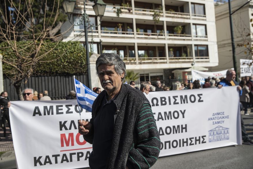 A protester holds a Greek flag during a demonstration outside the Interior Ministry in central Athens, on Thursday, Feb. 13, 2020. Regional government officials and residents from Lesbos and four other Aegean Sea islands oppose government plans to build new sites for migrants and refugees, and are demanding that thousands of asylum seekers at overcrowded camps on the islands be moved to the Greek mainland. The Moria refugee camp on the island of Lesbos currently has more than 20,000 people at a facility built for just 3,000 people. (AP Photo/Petros Giannakouris)