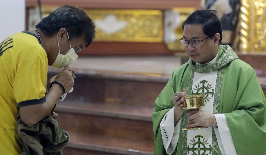 In this Feb. 10, 2020, photo, Catholic priest Fr. Joseph Arellano, right, looks at a man who forgot to take off his protective mask and tried to insert the host in his mouth during communion at a mass at the Minor Basilica of San Lorenzo Ruiz in Manila&#x27;s Chinatown, Philippines. In a popular Catholic church in Manila, nearly half of the pews were empty for Sunday Mass. The few hundred worshippers who showed up, some in protective masks, have been asked to refrain from shaking or holding hands in prayers. (AP Photo/Aaron Favila)