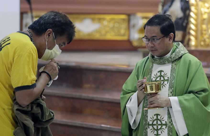 In this Feb. 10, 2020, photo, Catholic priest Fr. Joseph Arellano, right, looks at a man who forgot to take off his protective mask and tried to insert the host in his mouth during communion at a mass at the Minor Basilica of San Lorenzo Ruiz in Manila's Chinatown, Philippines. In a popular Catholic church in Manila, nearly half of the pews were empty for Sunday Mass. The few hundred worshippers who showed up, some in protective masks, have been asked to refrain from shaking or holding hands in prayers. (AP Photo/Aaron Favila)