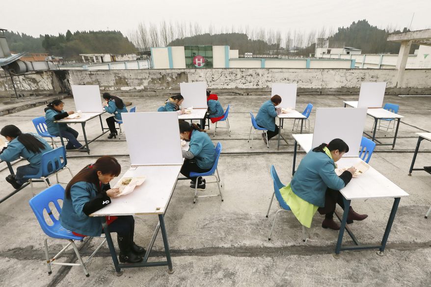 In this Friday, Feb. 14, 2020, photo, factory workers are separated by partitions as a precaution against infection as they take their lunch break on the roof of an electronics factory in Suining in southwestern China's Sichuan Province. China reported Saturday a figure of 2,641 new virus cases, a major drop from the higher numbers in recent days since a broader diagnostic method was implemented. (Chinatopix via AP)