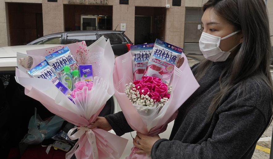 Flower shop owner Iris Leung wears her protective face mask as she delivers flowers with masks to customers on Valentine's Day in Hong Kong, Friday, Feb. 14, 2020. China has reported another sharp rise in the number of people infected with a new virus, as the death toll neared 1,400. (AP Photo/Vincent Yu)