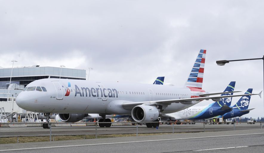 An American Airlines plane taxis past parked Alaska Airlines planes, Thursday, Feb. 13, 2020, at Seattle-Tacoma International Airport in Seattle. American Airlines and Alaska Airlines announced Thursday that they will cooperate more closely on West Coast service, including new American flights from Seattle to India's technology hub in Bangalore. (AP Photo/Ted S. Warren)