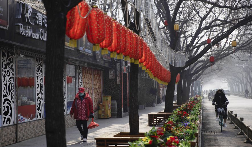 In this photo taken Tuesday, Feb. 11, 2020, a woman walks past Lunar New Year decor and shuttered bars at a retail district in Beijing, China. Millions of Chinese workers and entrepreneurs are bearing the rising costs of an anti-virus campaign that has shut down large sections of the economy. The government has imposed restrictions nationwide that have stalled travel and sales of real estate and autos. (AP Photo/Ng Han Guan)