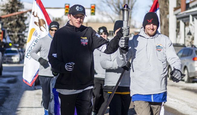 In this Feb. 4, 2020 photo Special Olympics athletes Brendan Burke and Gary Endecott carry the torch as they lead fellow athletes and and supporters down South Cache Street during the Law Enforcement Torch Run in Jackson, Wyo. The Special Olympics Wyoming Winter Games begin the next morning and ran through early Thursday afternoon with alpine skiing and snowboarding at Jackson Hole Mountain Resort and cross country skiing and snowshoeing at the town&#x27;s high school athletic fields. (Ryan Dorgan/Jackson Hole News &amp;amp; Guide via AP)