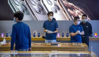 FILE - In a Feb. 14, 2020 file photo, employees wear face masks as they stand in a reopened Apple Store in Beijing. Apple Inc. is warning investors that it won&#x27;t meet its second-quarter financial guidance because the viral outbreak in China has cut production of iPhones. The Cupertino, California-based company said Monday, Feb. 17, 2020 that all of its iPhone manufacturing facilities are outside Hubei province, and all have been reopened, but production is ramping up slowly. (AP Photo/Mark Schiefelbein, File)