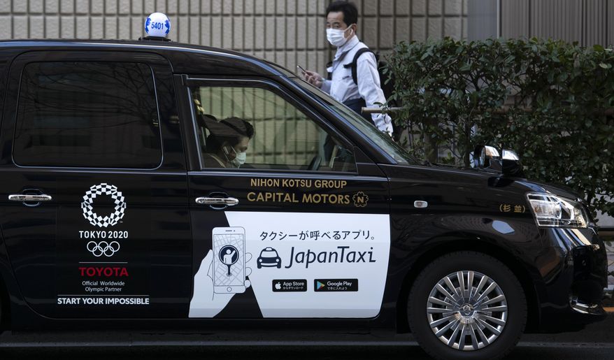 A taxi driver wearing a mask waits for a fare with a Tokyo 2020 logo on the door of his cab Tuesday, Feb. 18, 2020, in Tokyo. Tokyo Olympic organizers said last week there is no "Plan B" for the 2020 Games, which open in just over five months and have been jolted by the outbreak of a virus in neighboring China. (AP Photo/Jae C. Hong)
