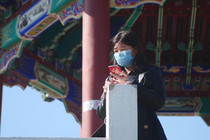 A woman wearing a face mask stands at a pagoda in Ritan Park in Beijing, Tuesday, Feb. 18, 2020. A hospital director who helped lead the fight against China's new virus has become one of its victims. His death comes as authorities are cautiously cheering a reduction in the number of new daily cases and deaths, along with the results of a study showing most people who contract the virus experience only mild symptoms. (AP Photo/Sam McNeil)