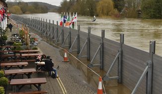People eating at a pub in front of temporary flood defences set up in the aftermath of Storm Dennis, in Bewdley, England, Wednesday Feb. 19, 2020. Flood-hit communities are braced for further heavy rain as river levels continue to threaten to breach barriers. (Jacob King/PA via AP)
