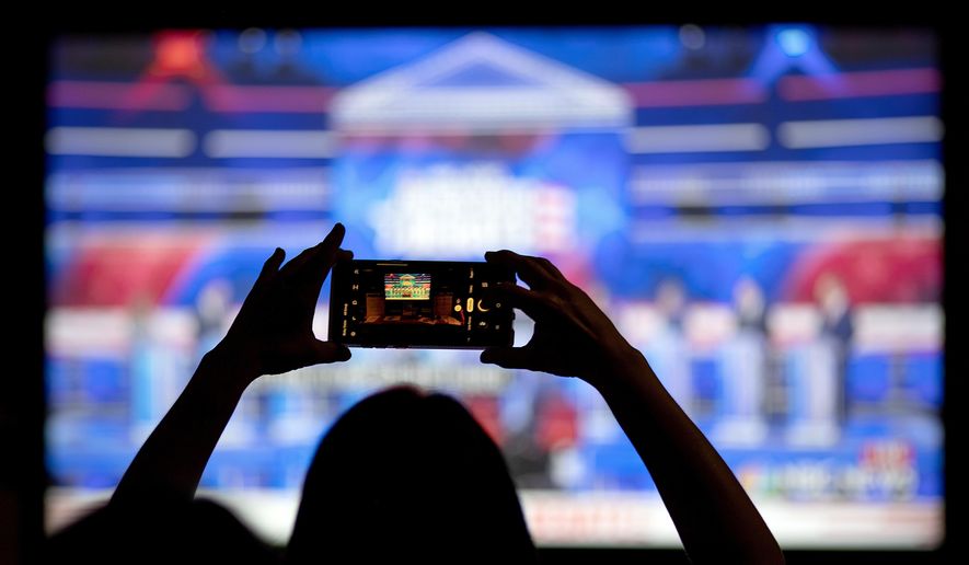 FILE - In this June 27, 2019, file photo, a woman takes a photo of the television while watching a Democratic presidential debate at a watch party in Atlanta. The Democratic race for the White House has been marked by online infighting and unsubstantiated allegations of election rigging. (AP Photo/David Goldman, File)