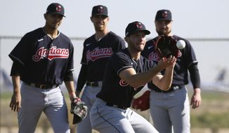 Cleveland Indians pitcher Kyle Dowdy, front, fields a grounder as pitchers Carlos Carrasco, left, Shane Bieber, middle, and Logan Allen, right, look on during spring training baseball workouts for pitchers and catchers Thursday, Feb. 13, 2020, in Avondale, Ariz. (AP Photo/Ross D. Franklin)