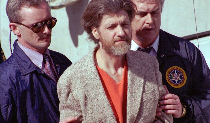 FILE — In this April 4, 1996 file photo Theodore John Kaczynski is flanked by federal agents as he is led to a car from the federal courthouse in Helena, Mont. A federal grand jury in San Francisco indicted Vladislav Victorvic Timoshchuk, on charges of mailing two envelopes containing ricin to Pelican Bay State Prison, officials announced on Friday Feb. 21, 2020. Last year the federal Bureau of Prisons intercepted a Christmas card from Timoshchuk, now living in Belarus, to Kaczynski, the convicted Unabomber, which authorizes say Timoshchuk discussed his plan to mail ricin to the United States. Kaczynski is serving a life sentence in a federal prison in Colorado for carrying out a series of mail bombings that killed three people. (AP Photo/John Youngbear, File)