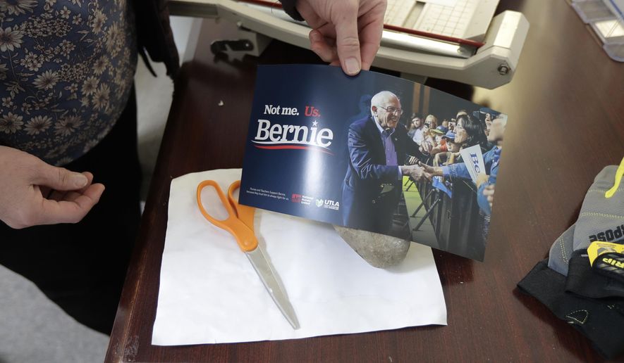 Carin Chase, director of Washington state for the campaign of Democratic presidential candidate Sen. Bernie Sanders, I-Vt., uses a Sanders campaign sign to cover a rock Saturday, Feb. 22, 2020, in Seattle that was used to break the glass of the door to Sanders' Seattle headquarters Friday night as she makes a humorous reference to a "rock-paper-scissors" game. Police are investigating, but no one was hurt in the vandalism incident, and campaign workers swept up the pieces and patched the door with plywood. (AP Photo/Ted S. Warren)