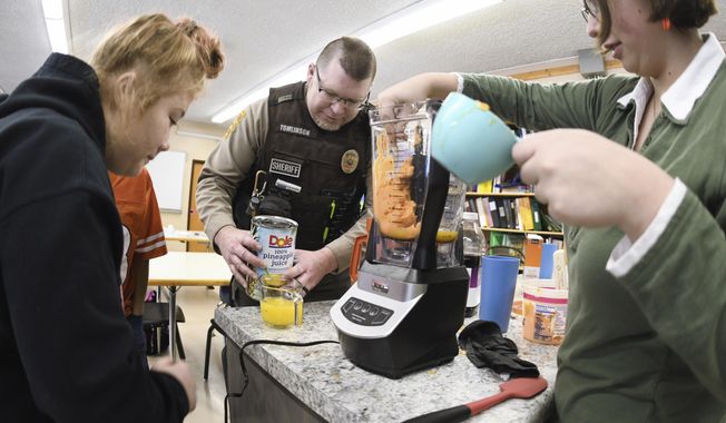 Morton County Deputy Sheriff David Tomlinson helps students Erica Simpson, 16, left, and Sabrina Doll, 15, make a slushy juice drink during his visit on Jan. 30, 2020 to New Salem High School in New Salem, North Dakota.  (Mike McCleary/The Bismarck Tribune via AP)
