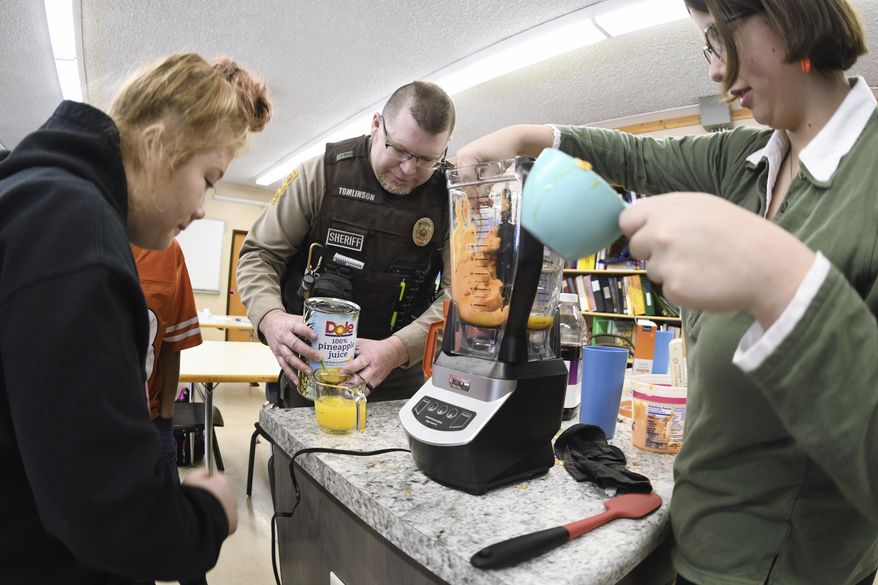 Morton County Deputy Sheriff David Tomlinson helps students Erica Simpson, 16, left, and Sabrina Doll, 15, make a slushy juice drink during his visit on Jan. 30, 2020 to New Salem High School in New Salem, North Dakota.  (Mike McCleary/The Bismarck Tribune via AP)