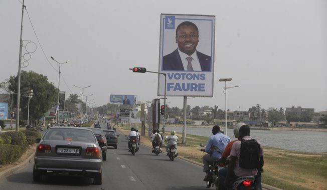Cars drive past election posters of Togo's Incumbent President Faure Gnassingbe, Presidential Candidate of Union for the Republic, on the street in Lome, Togo Friday, Feb. 21, 2020. The West African nation of Togo is voting Saturday in a presidential election that is likely to see the incumbent re-elected for a fourth term despite years of calls by the opposition for new leadership. (AP Photo/Sunday Alamba)