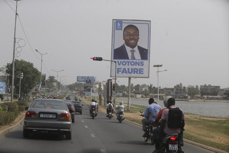 Cars drive past election posters of Togo's Incumbent President Faure Gnassingbe, Presidential Candidate of Union for the Republic, on the street in Lome, Togo Friday, Feb. 21, 2020. The West African nation of Togo is voting Saturday in a presidential election that is likely to see the incumbent re-elected for a fourth term despite years of calls by the opposition for new leadership. (AP Photo/Sunday Alamba)